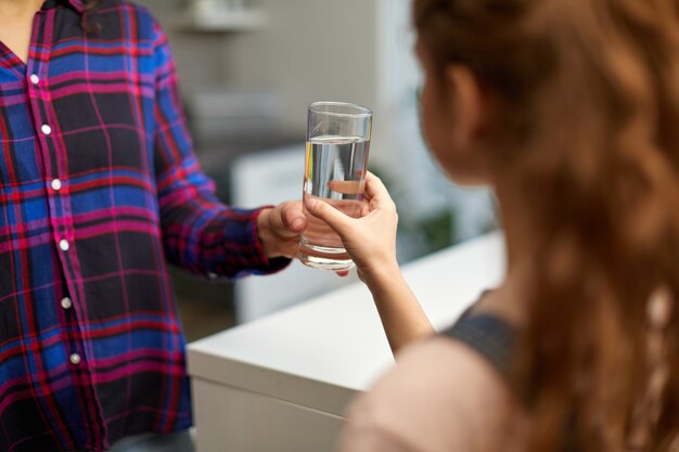 Imagen recortada de una niña sosteniendo un vaso de agua en la cocina con la joven madre.