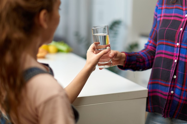 Imagen recortada de una niña sosteniendo un vaso de agua en la cocina con la joven madre.