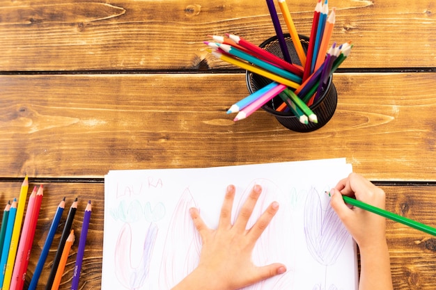 Foto imagen recortada de un niño dibujando en papel con lápices de colores en la mesa
