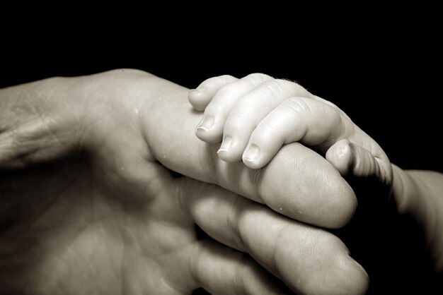 Foto imagen recortada de un padre sosteniendo la mano de su bebé contra un fondo negro