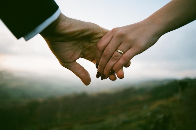 Imagen recortada de una pareja tomándose de la mano contra el cielo