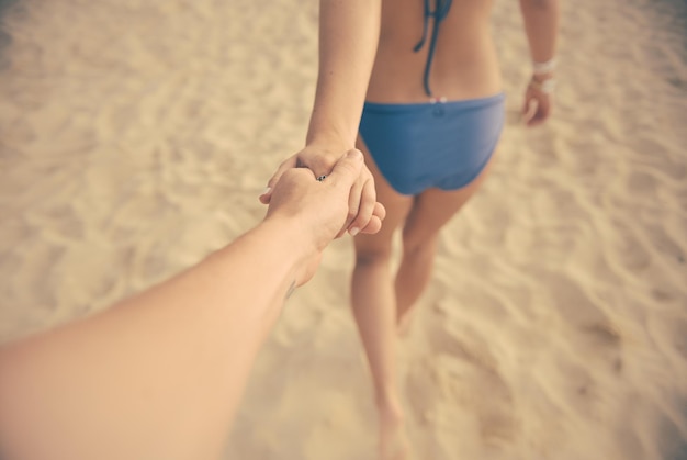 Imagen recortada de una pareja tomándose de la mano en la playa