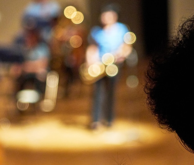 Foto imagen recortada de una persona frente a músicos desenfocados actuando en un concierto