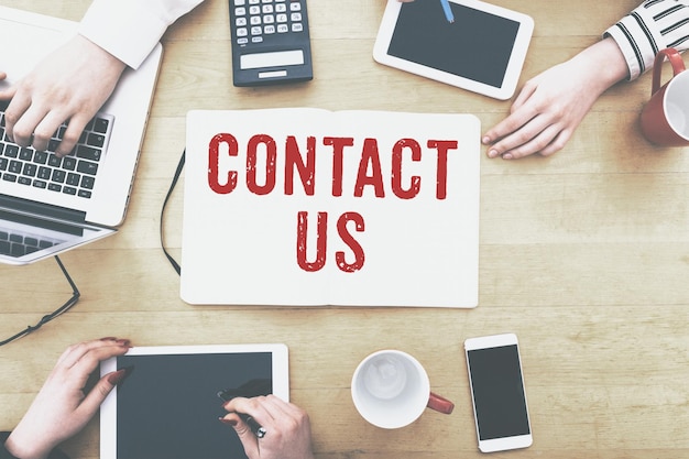 Imagen recortada de personas de negocios con tecnologías en medio de texto de contacto en el escritorio