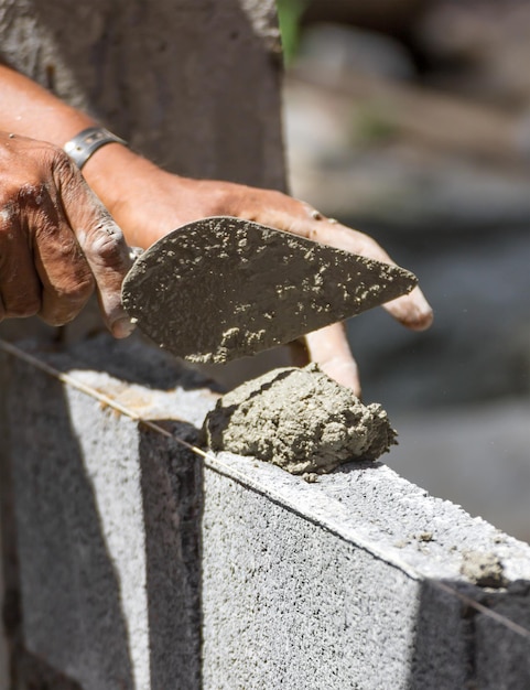 Foto imagen recortada de un trabajador de la construcción poniendo cemento en una pared de piedra