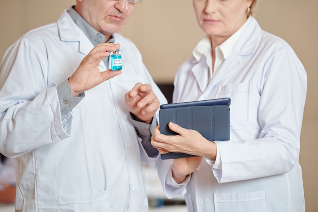 Imagen recortada de trabajadores médicos con el artículo de lectura de la vacuna covid-19 en una tableta