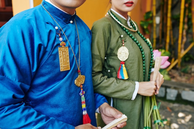 Imagen recortada de vietnamitas recién casados con vestidos ao dai caminando al aire libre después de la boda