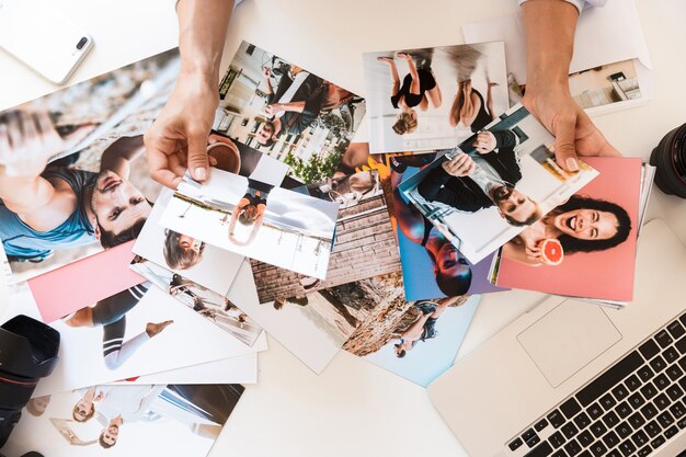 Imagen recortada de la vista superior de una joven fotógrafa en la mesa sosteniendo fotos.