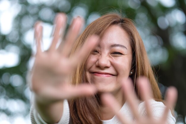 Imagen de retrato de una hermosa joven asiática levantando las manos y jugando con la cámara en el parque