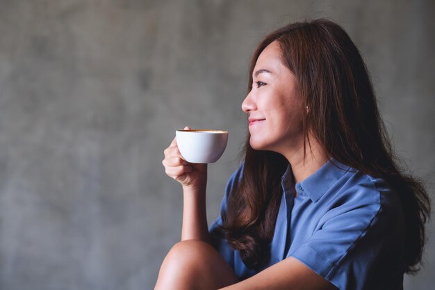 Imagen de retrato de una hermosa joven asiática sosteniendo y bebiendo café caliente