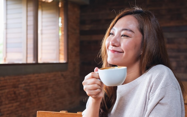 Imagen de retrato de una hermosa joven asiática sosteniendo y bebiendo café