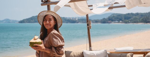 Imagen de retrato de una hermosa joven asiática sosteniendo y bebiendo jugo de coco en la playa