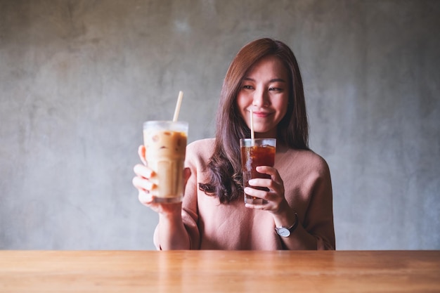 Imagen de retrato de una hermosa mujer asiática sosteniendo y bebiendo dos vasos de café helado
