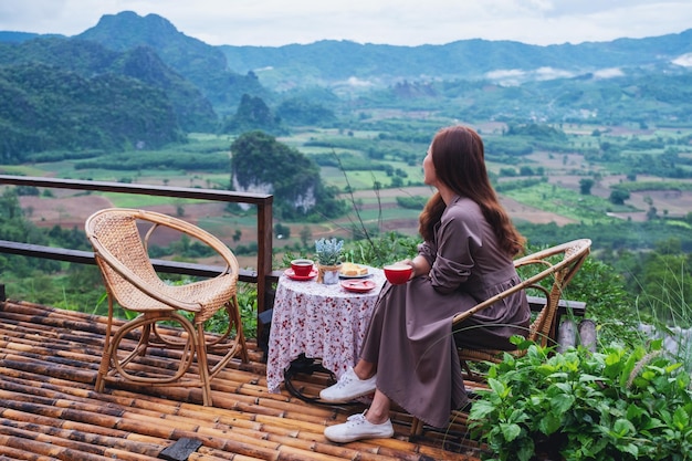 Imagen de retrato de una hermosa mujer bebiendo café caliente en el balcón mientras mira las montañas y la naturaleza verde