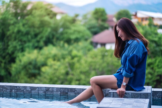 Imagen de retrato de una joven y bella mujer asiática disfrutó de sentarse junto a la piscina con fondo de naturaleza verde