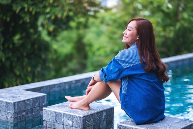 Imagen de retrato de una joven y bella mujer asiática disfrutó de sentarse junto a la piscina con fondo de naturaleza verde