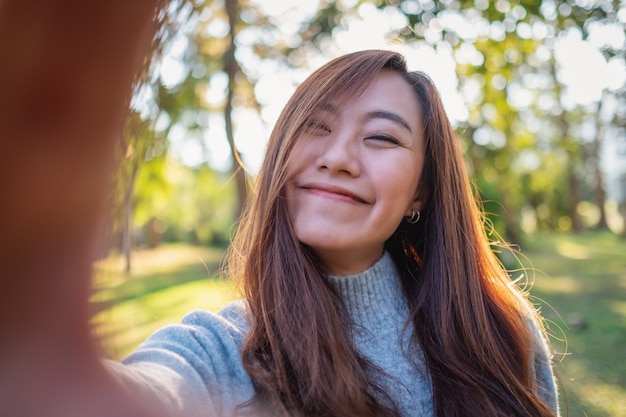 Imagen de retrato de una mujer asiática hermosa feliz haciendo foto selfie en el parque