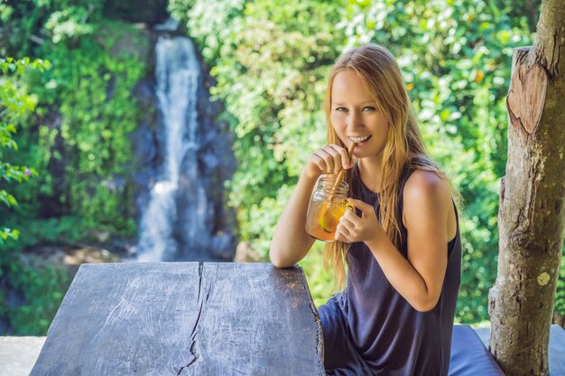 Imagen de retrato de primer plano de una mujer hermosa bebiendo té helado con una sensación de felicidad en la naturaleza verde y el fondo del jardín de la cascada