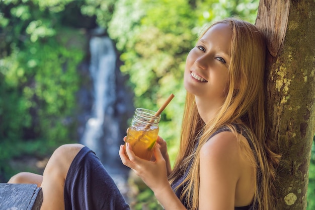 Imagen de retrato de primer plano de una mujer hermosa bebiendo té helado con una sensación de felicidad en la naturaleza verde y el fondo del jardín de la cascada