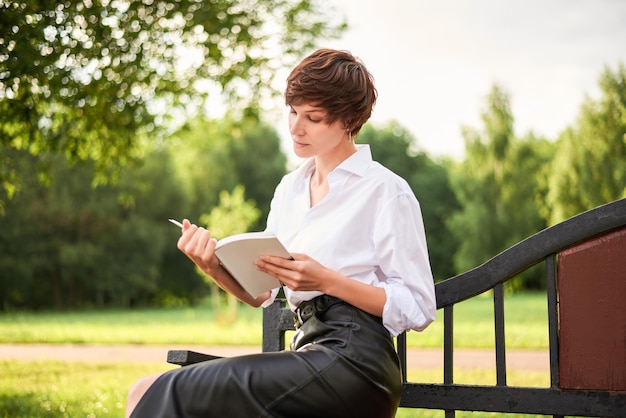 Imagen retro de una mujer elegante y hermosa sentada en un parque en un banco con un libro en las manos El concepto de estilo y moda