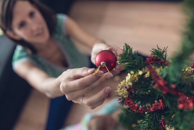 Imagen retro vintage de una mujer joven sentada en el suelo colocando adornos navideños rojos en un pequeño árbol navideño.