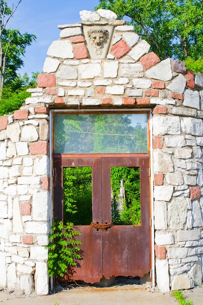 Imagen de las ruinas de una antigua torre de piedra con una puerta oxidada que ha sido cubierta de árboles en el fondo