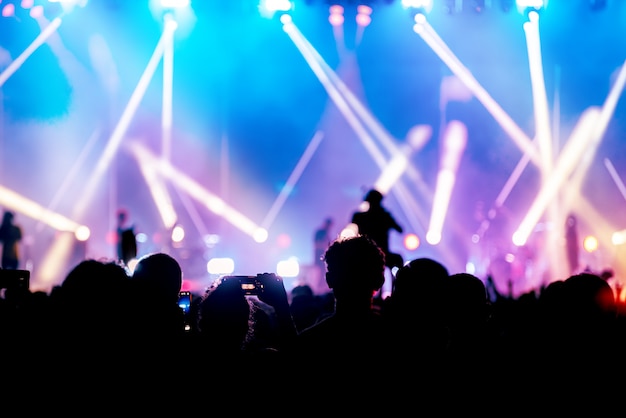 Imagen de la silueta y desenfocada de la iluminación colorida del concierto de entretenimiento en el escenario, audiencia que toma fotos del artista, concierto en vivo borroso y fiesta en la discoteca.