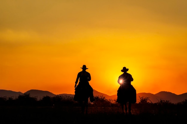Imagen de silueta de dos vaqueros a caballo al atardecer con el fondo de la cordillera