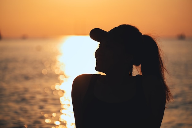 Imagen de silueta de una mujer sentada y viendo la puesta de sol junto al mar