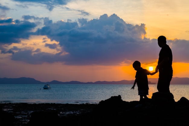 Imagen de la silueta del padre y el hijo en la playa antes del fondo del atardecer