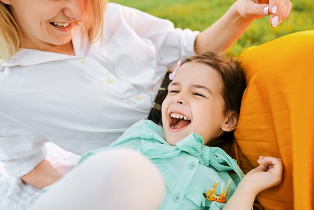 Imagen sincera de primer plano de un niño feliz jugando con su madre disfrutando el tiempo juntos Linda niña riendo con mamá sentada en el césped en el parque Madre e hija comparten amor Infancia