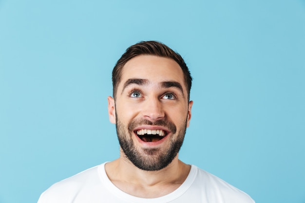 Imagen de soñar sonriente joven barbudo feliz posando aislado sobre pared azul mirando a un lado. Concepto de verano.