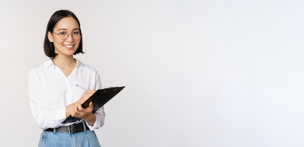 Imagen de una sonriente empleada coreana de la oficina escribiendo en el portapapeles tomando notas de pie