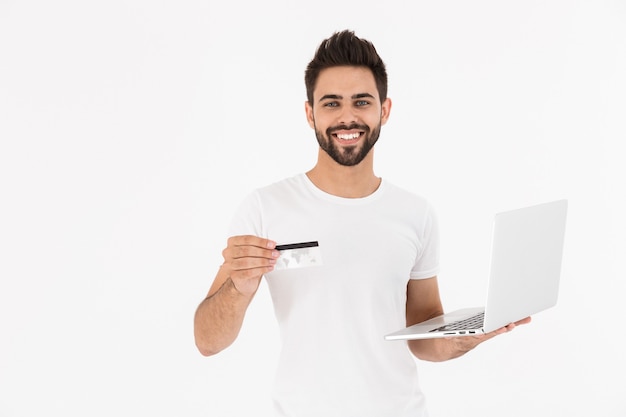 Imagen de sonriente hombre complacido con tarjeta de crédito y portátil aislado sobre pared blanca