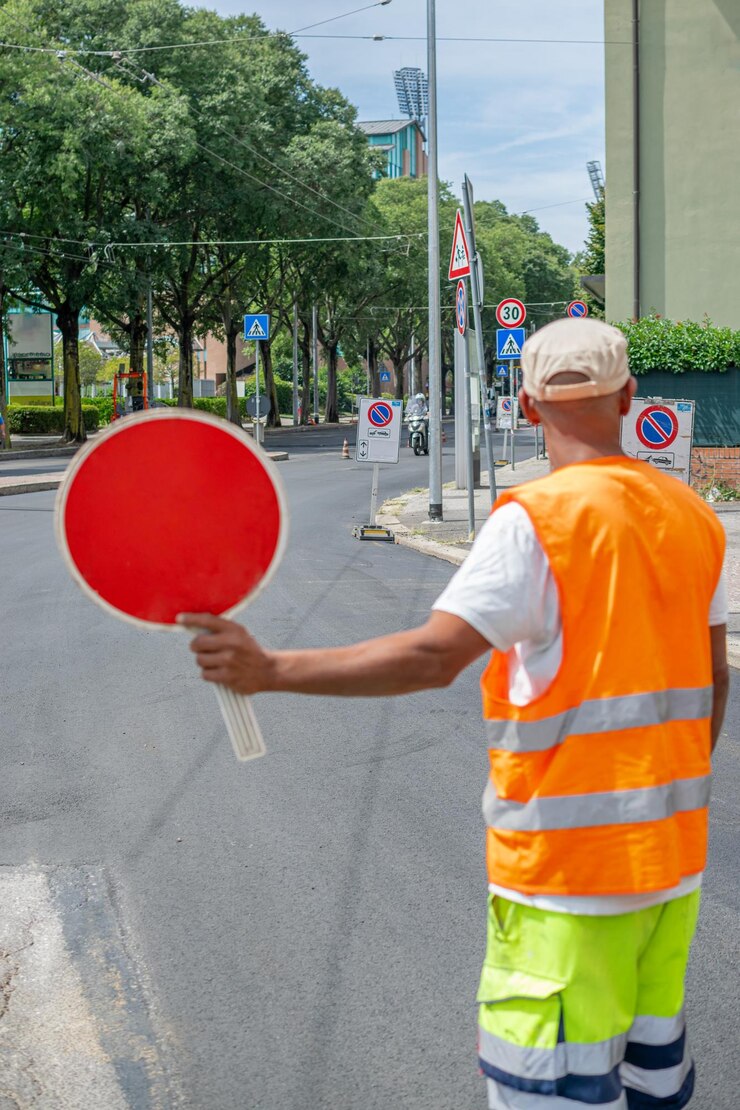Imagen de un trabajador de la construcción sosteniendo una señal de alto roja y dirigiendo el tráfico en la calle