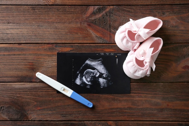 Imagen de ultrasonido de la prueba de embarazo del bebé y zapatos para niños sobre fondo de madera