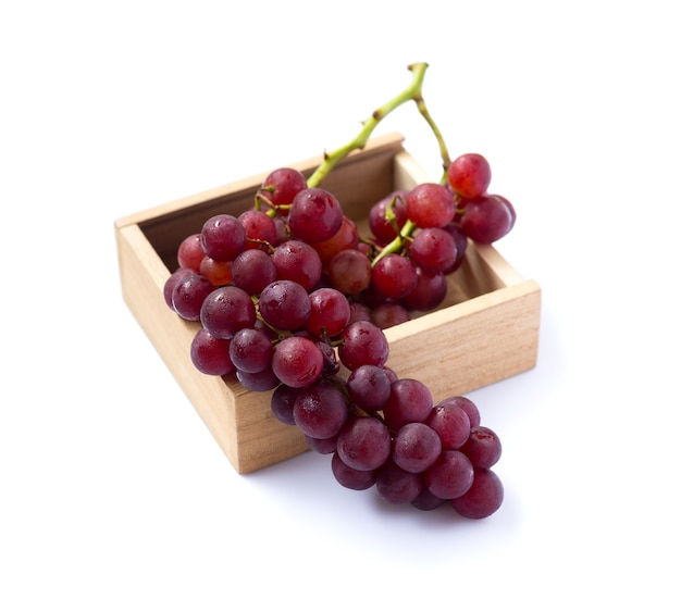 Imagen de uvas rojas en una caja de madera aislada sobre fondo blanco
