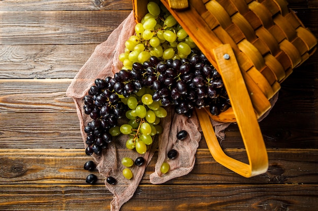 Imagen de uvas verdes y negras en cesta de madera en la mesa