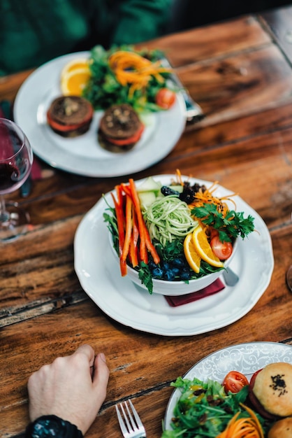 Imagen vertical de una cena vegetariana servida en una mesa de madera en un restaurante Hamburguesa vegetariana deliciosa y ensalada orgánica mixta en un plato blanco
