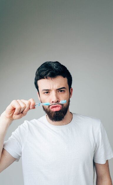 Imagen vertical de chico pacífico divertido serio jugando con cepillo de dientes. sostenlo entre la boca y la nariz. concepto de salud