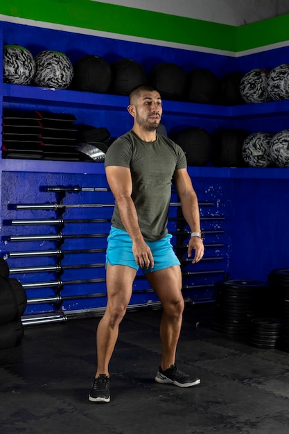 Imagen vertical de un hombre latino haciendo sentadillas con ropa deportiva en un gimnasio de crossfit