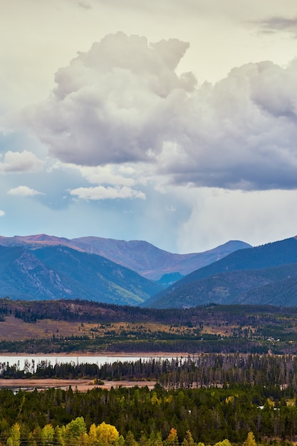 Imagen de la vertical de las montañas con nubes de lluvia y agua con pinos que rodean