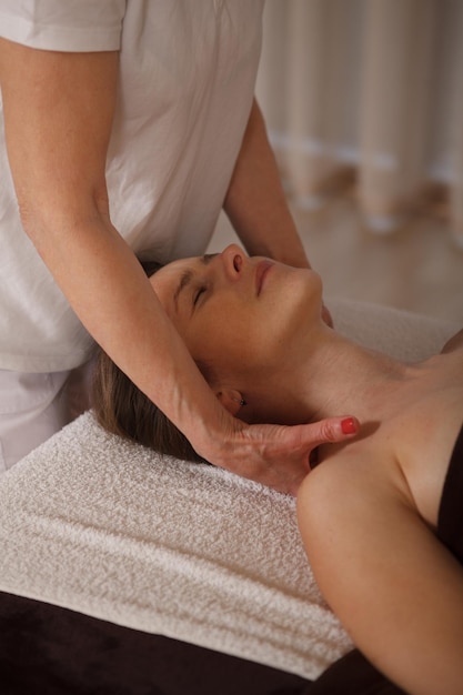Imagen vertical de una mujer madura relajada que disfruta de un masaje profesional en los hombros