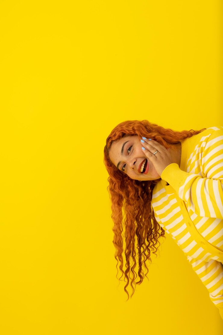 Imagen vertical de una mujer pelirroja mirando felizmente en un fondo amarillo