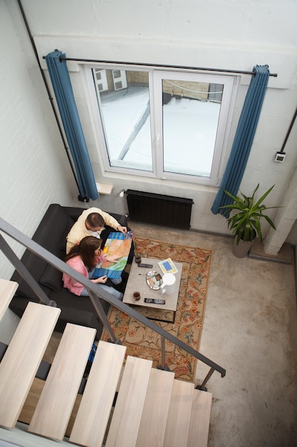 Imagen vertical de una pareja examinando el mapa de la ciudad sentada en un sofá en su habitación de albergue