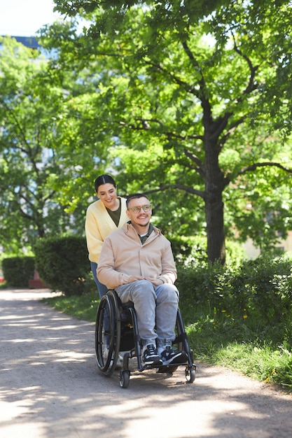 Imagen vertical de una pareja joven con un hombre con discapacidad caminando juntos en el parque en verano