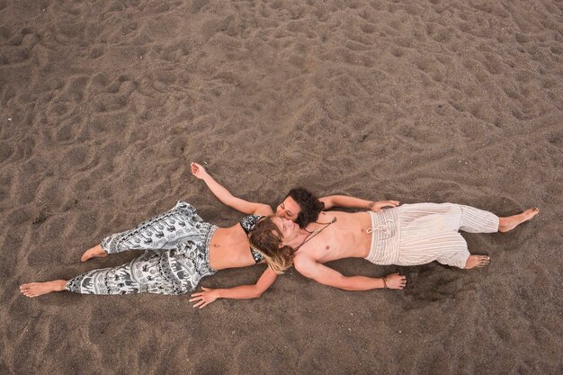 Imagen de vista aérea de una joven y alegre pareja tumbada en la playa en la arena, relájese y disfrute de la temporada de verano con ropa étnica y hippy de vacaciones para gente agradable en vacaciones