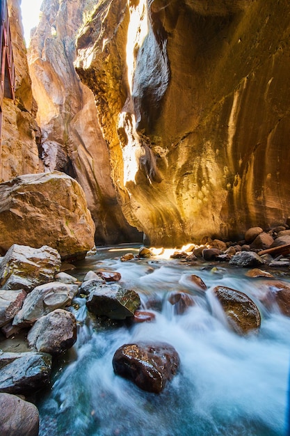 Imagen de vista cercana de cascadas sobre rocas rojas en la parte inferior del cañón profundo con luz solar dorada