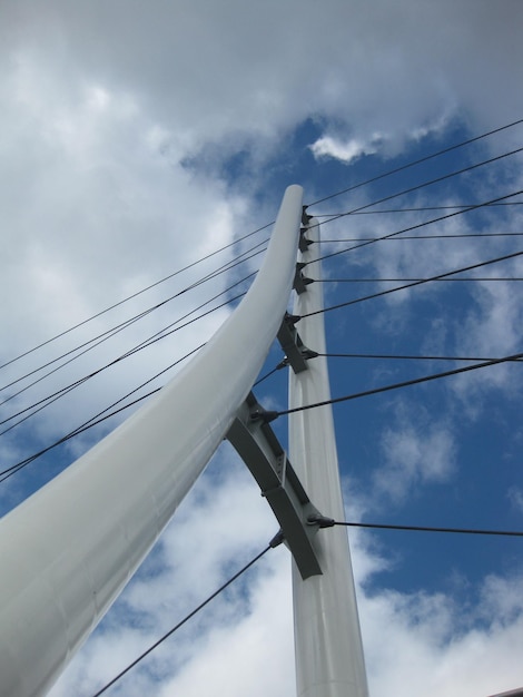 Imagen de la vista de gusano de un puente triangular blanco con cables de suspensión cruzando un cielo azul y nublado