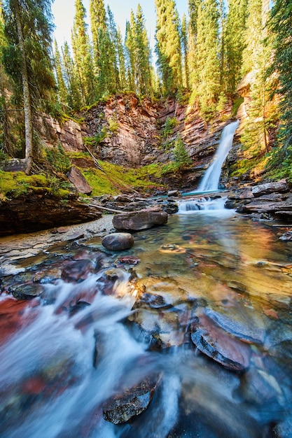 Imagen de la vista por el lecho del río poco profundo con una hermosa cascada en la distancia escondida en un colorido cañón cubierto de musgo